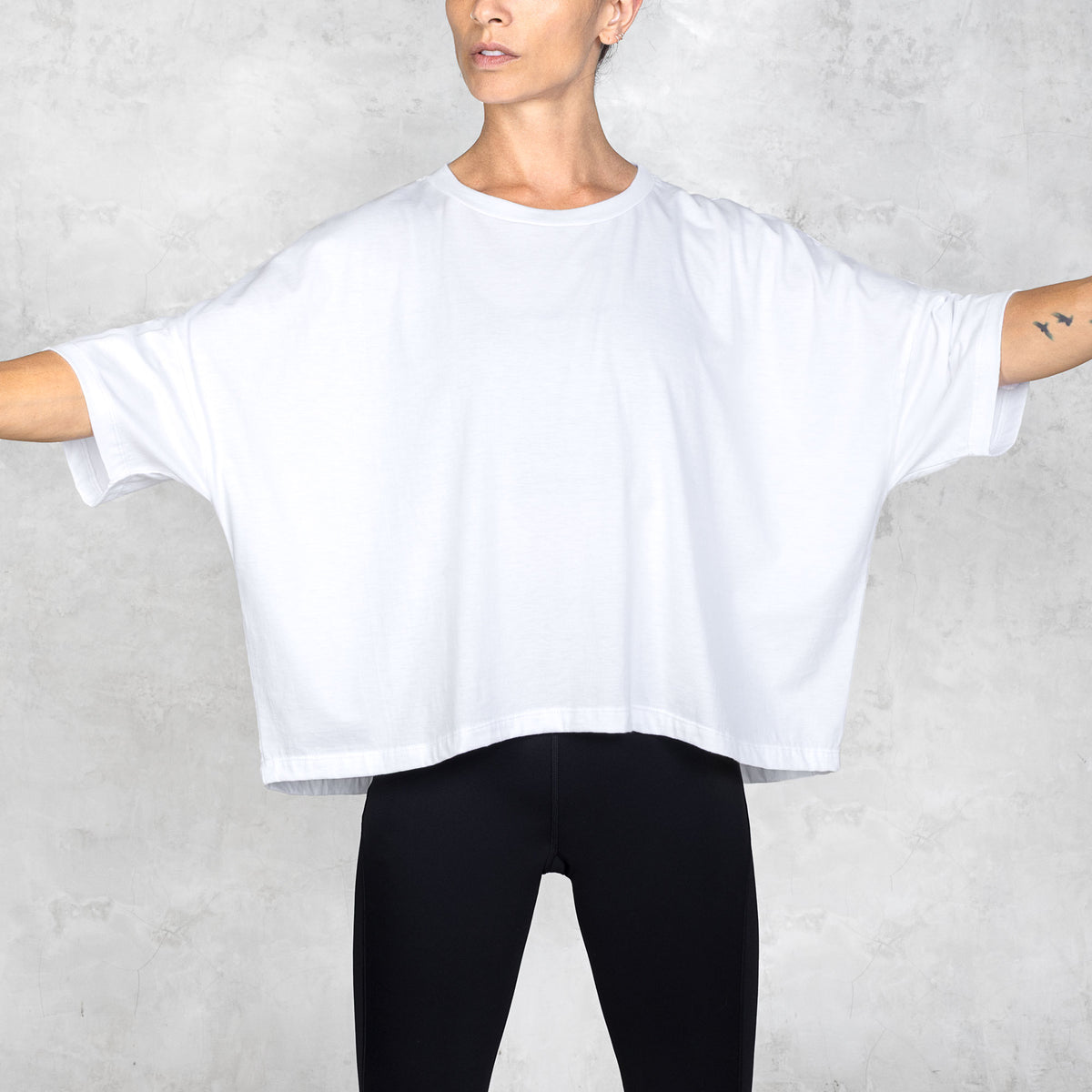 Person wearing a white oversized t-shirt and black pants against a white background