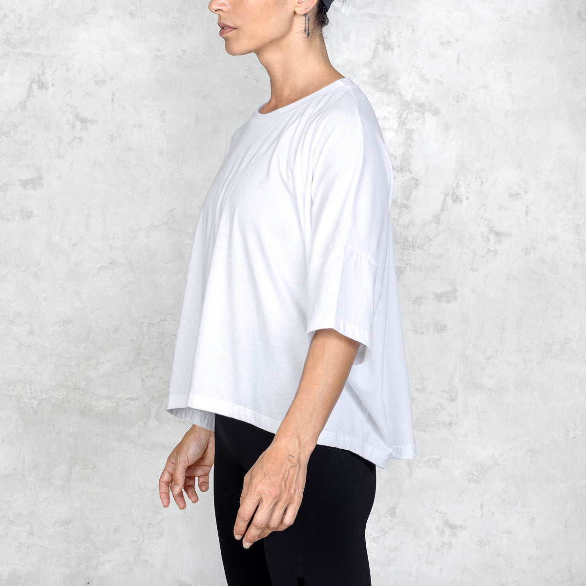 Side view of a person wearing a white oversized t-shirt and black pants against a white background