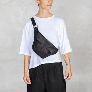 Person wearing a white t-shirt, black pants, and a black sling bag over one shoulder against a plain background