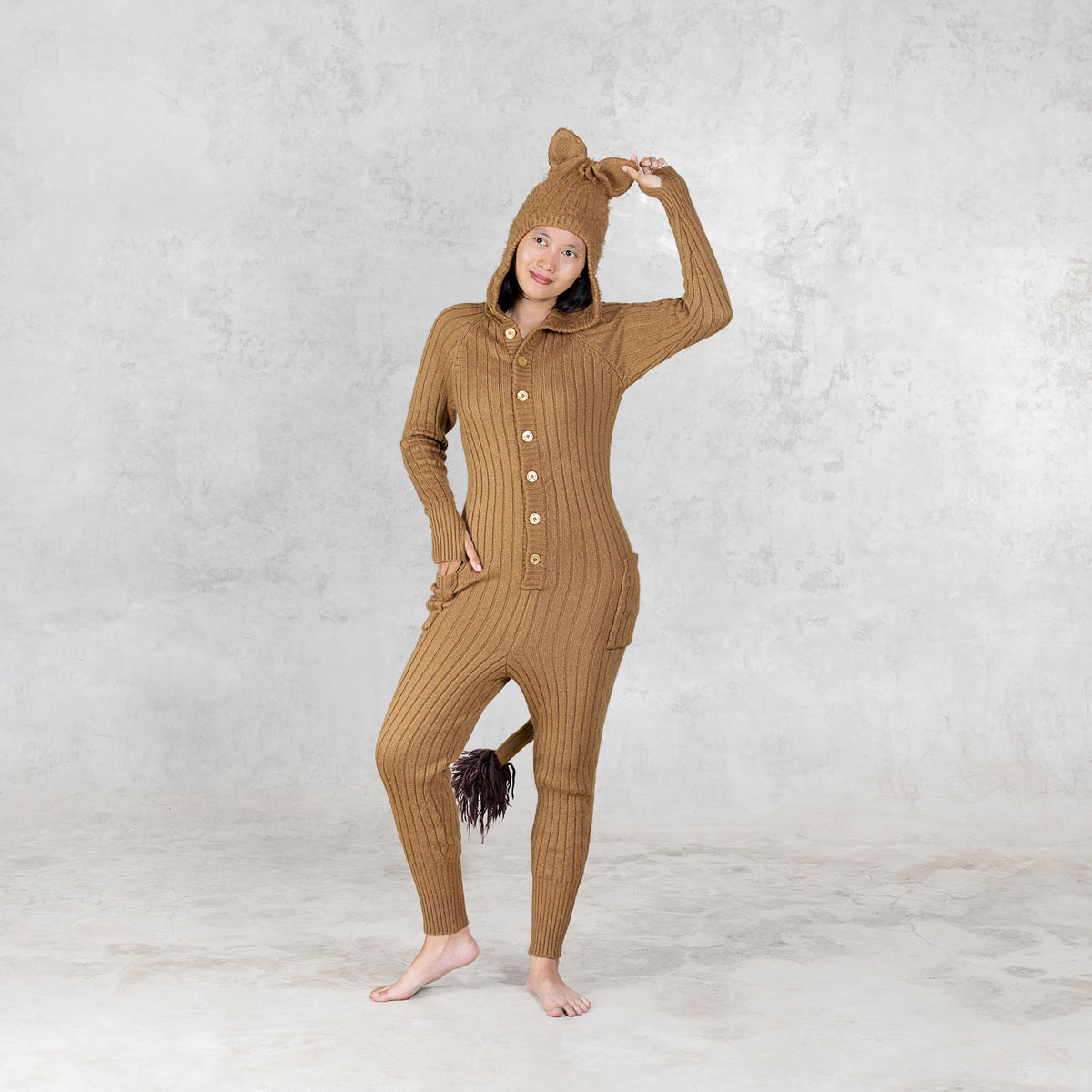 Person wearing a brown ribbed lion onesie with a hood against a light gray background