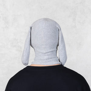 Person wearing a knit gray hood with long ears against a light gray background 