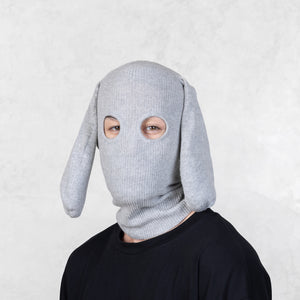 Person wearing a gray knit balaclava with floppy ears against a light gray background 