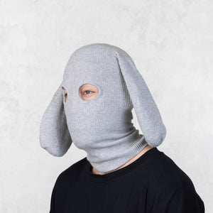 Person wearing a gray knitted dog mask against a light background