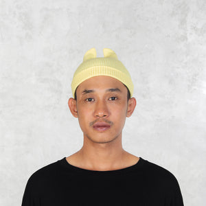 Person wearing a light yellow beanie with spikey ears against a plain background