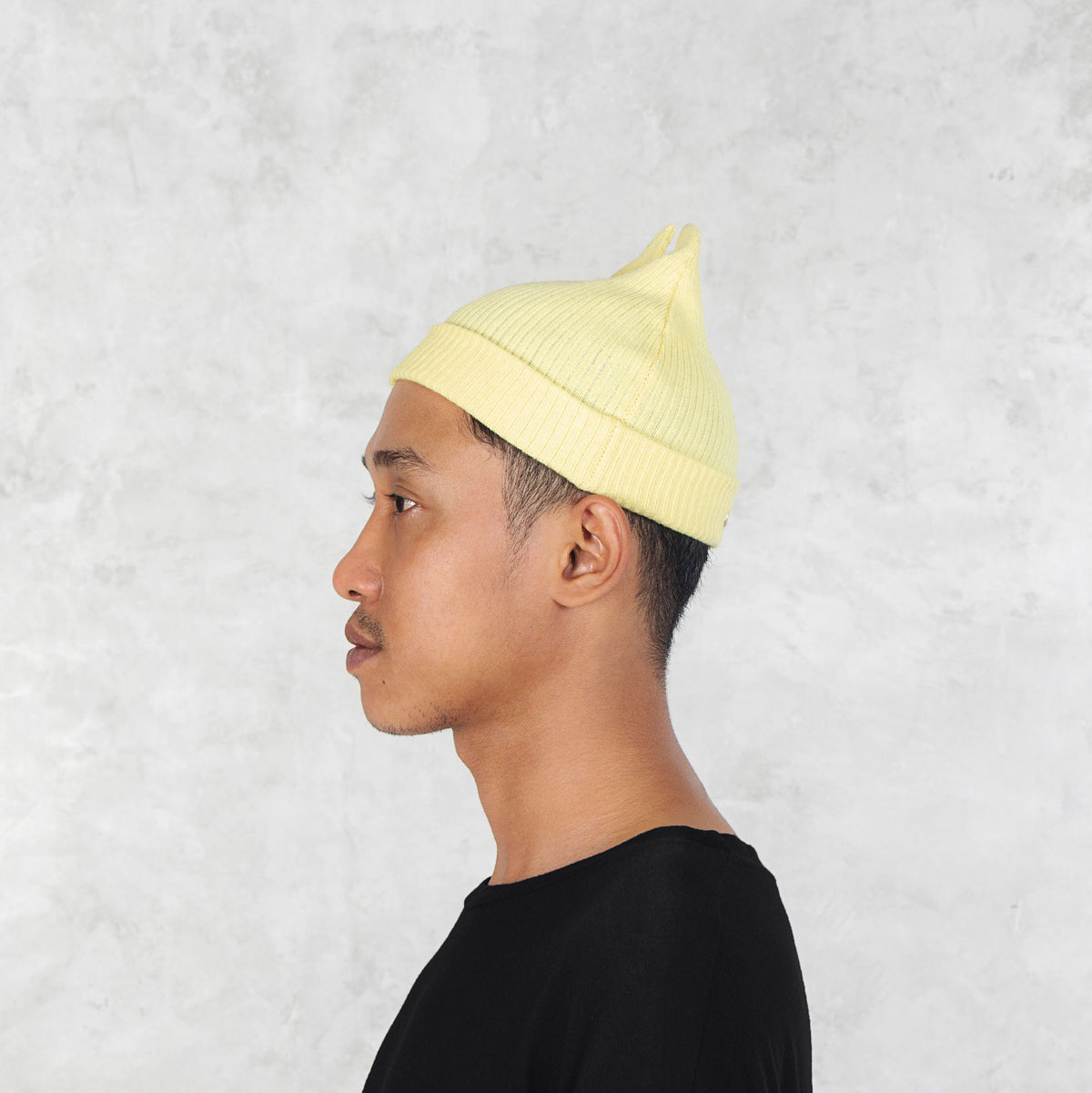 Person facing sideways wearing a light yellow beanie with spikey ears against a plain background