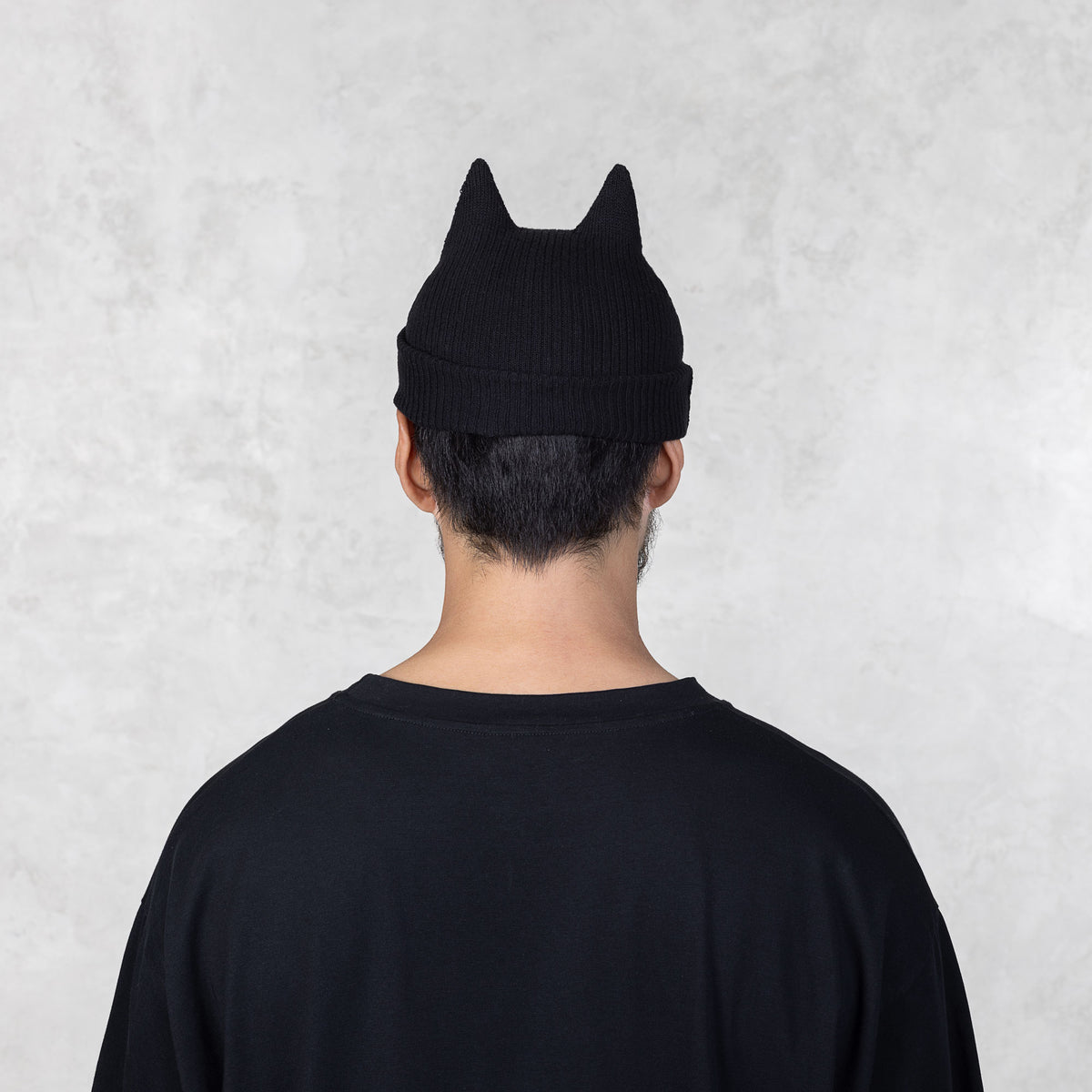 Person facing backwards wearing a black beanie with spike ears against a light gray background