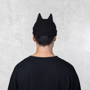 Person facing backwards wearing a black beanie with spike ears against a light gray background