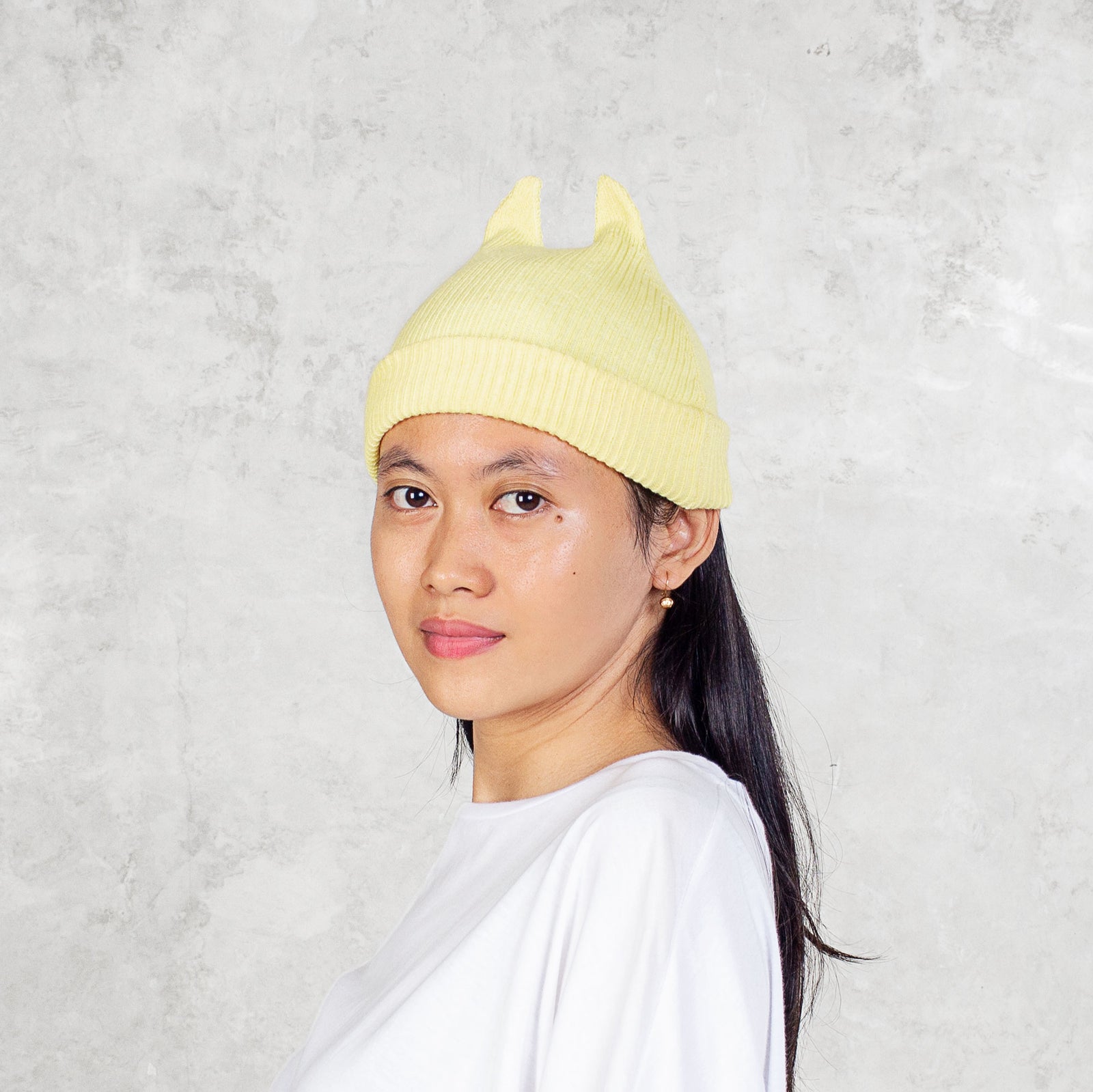 Person wearing a yellow beanie with spikey ears against a light gray background