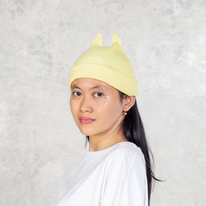 Person wearing a yellow beanie with spikey ears against a light gray background