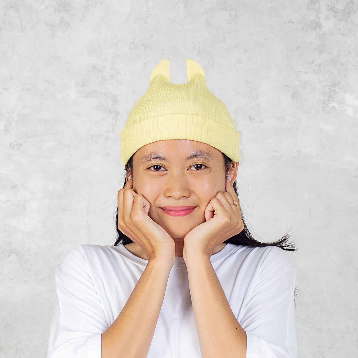 Person smiling wearing a yellow knit hat with spikey ears against a light gray background