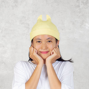 Person smiling wearing a yellow knit hat with spikey ears against a light gray background