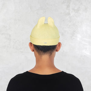 Person facing backwards wearing a yellow knit hat with spikey ears on a light gray background
