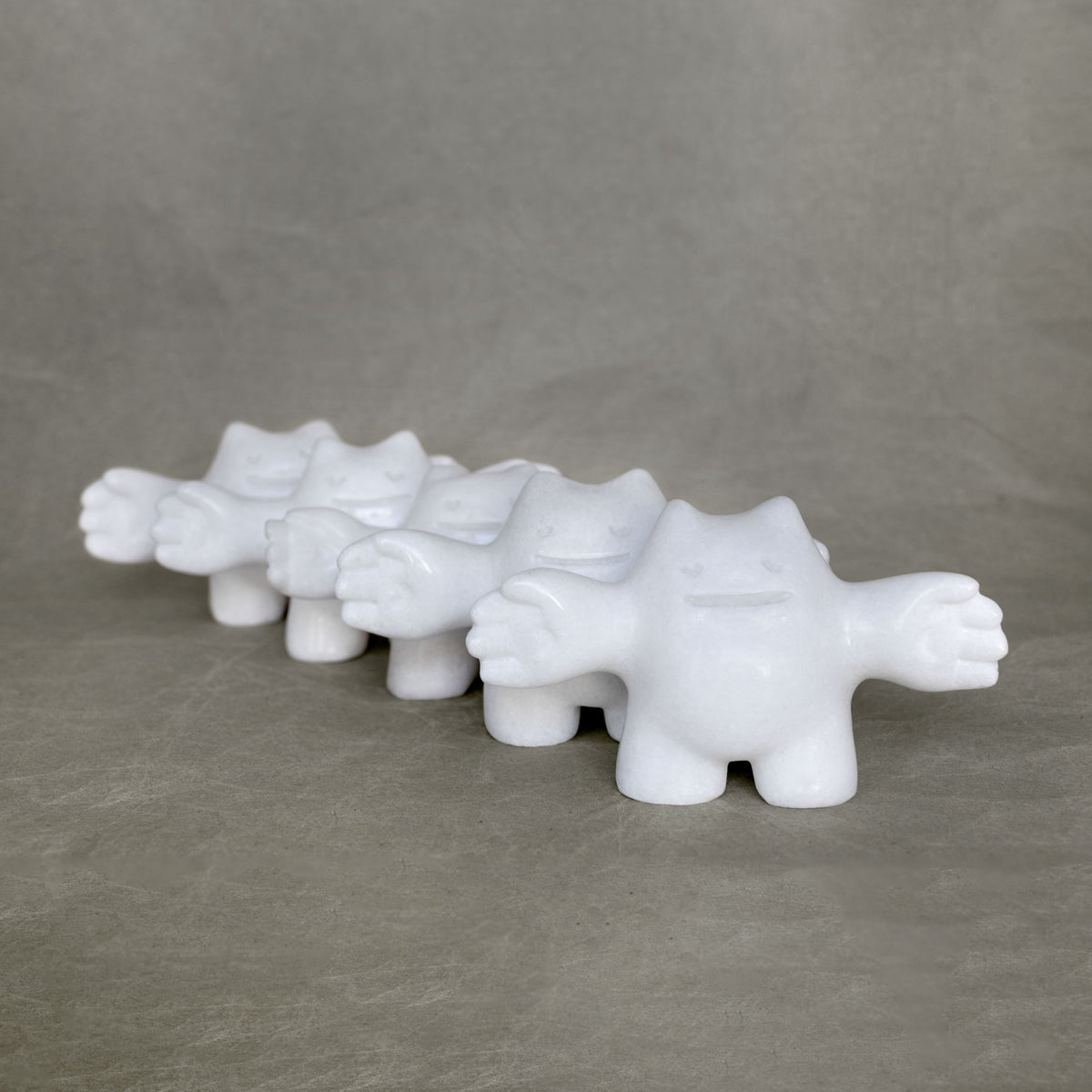Group of small marble creature figurines with their arms stretched outwards against a gray background