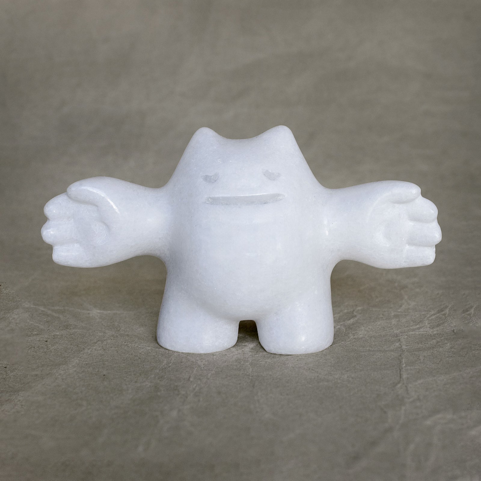 White marble sculpture of a creature with outstretched arms on a gray background
