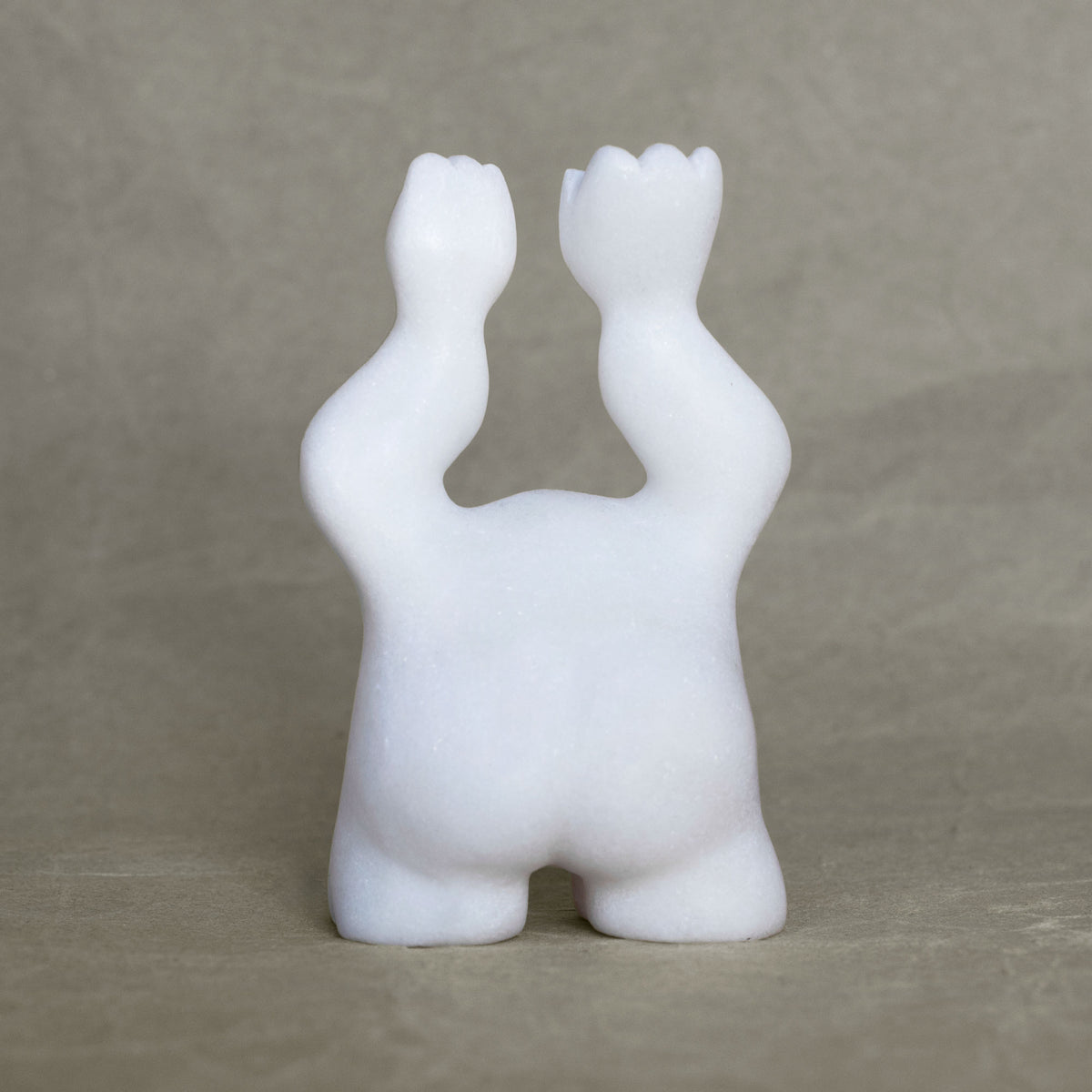 Back view of a small marble creature figurine with its arms raised above its head against a gray background