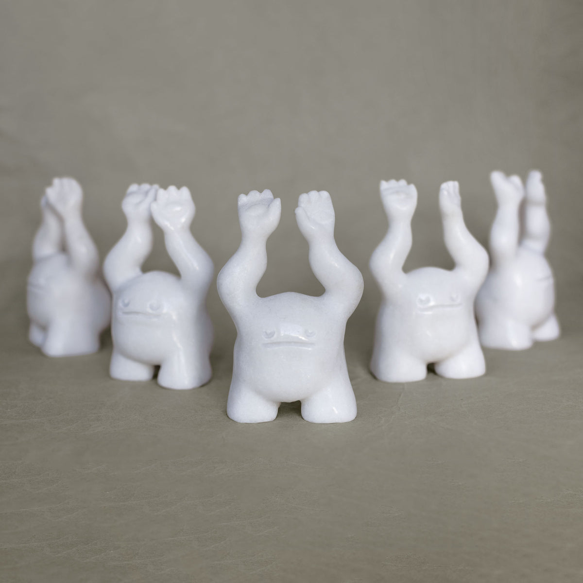 Group of small marble creature figurines with its arms raised above their heads against a gray background