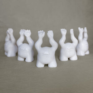 Group of small marble creature figurines with its arms raised above their heads against a gray background