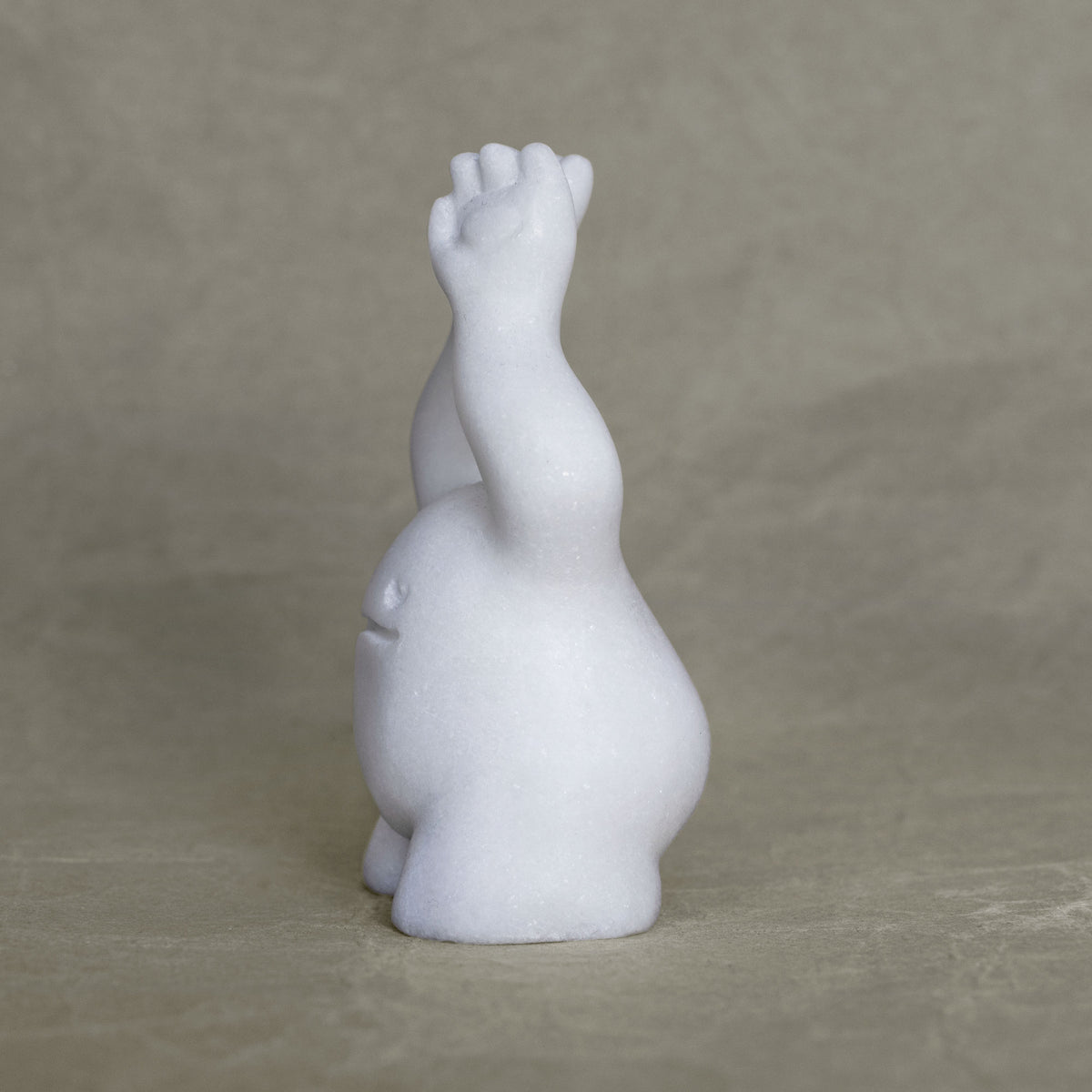 Side view of a small marble creature figurine with its arms raised above its head against a gray background