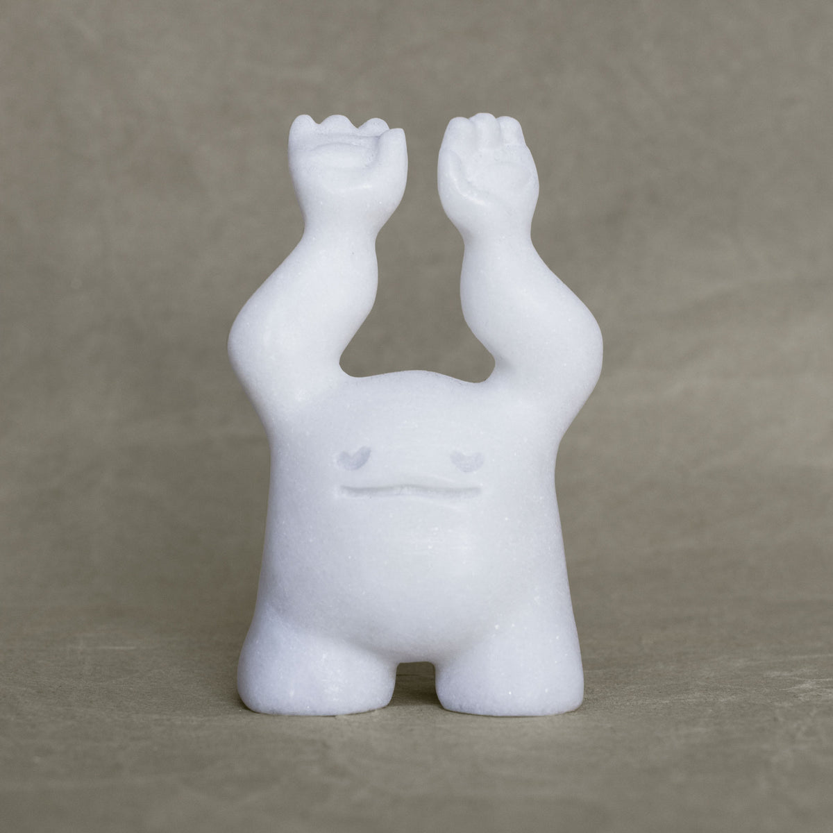 Small marble creature figurine with its arms raised above its head against a gray background