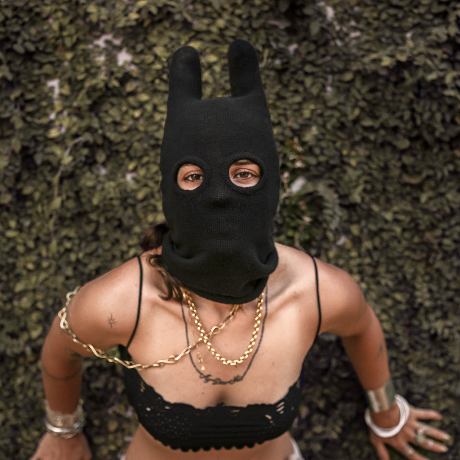 Person wearing a black mask with ears and gold jewelry against a natural backdrop