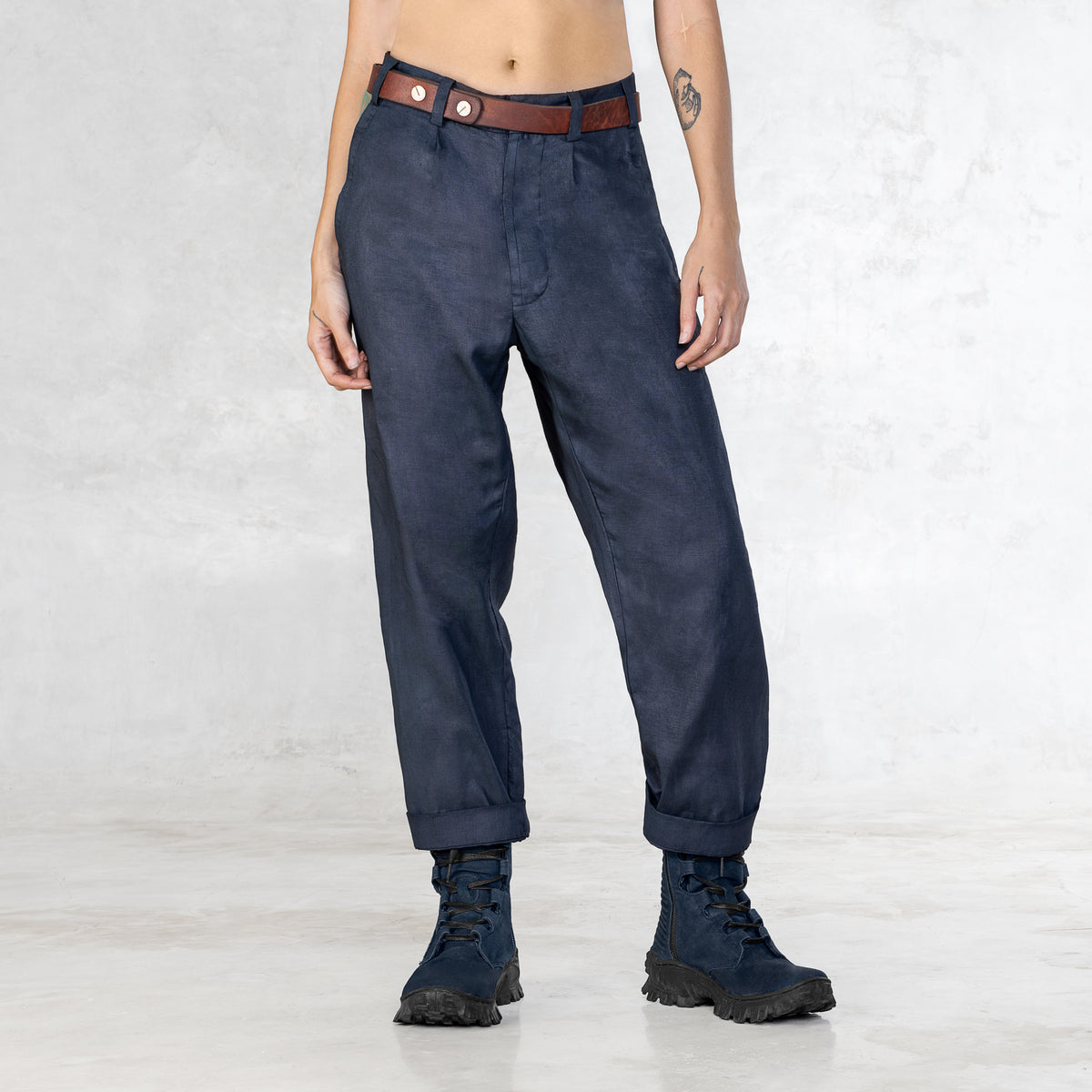 A woman standing  from the waist down in Indigo pants and no shirt with a brown leather belt