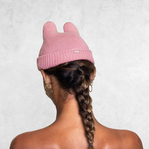 Woman from the chest up facing back wearing a small pink beanie with little horns