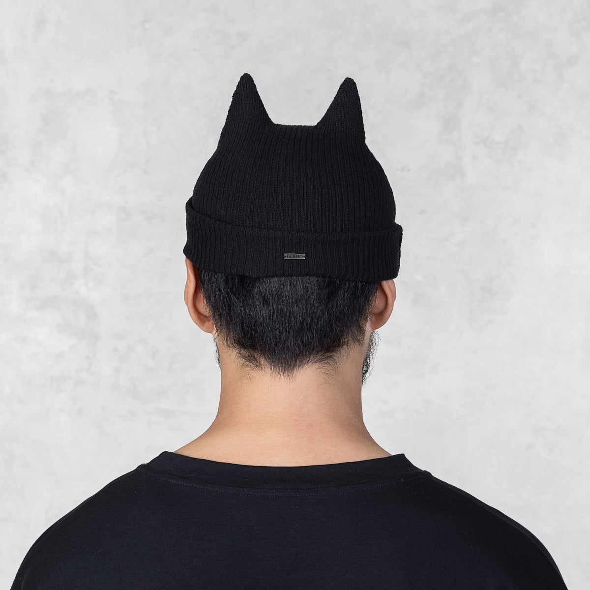 Person wearing a black beanie with cat ears on a light gray background