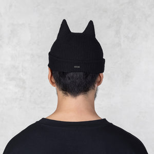 Person wearing a black beanie with cat ears on a light gray background