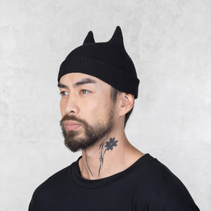 Man wearing a black beanie with cat ears against a light gray background