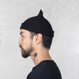 Man wearing a Blamo Mini Spike black knit beanie against a light gray background