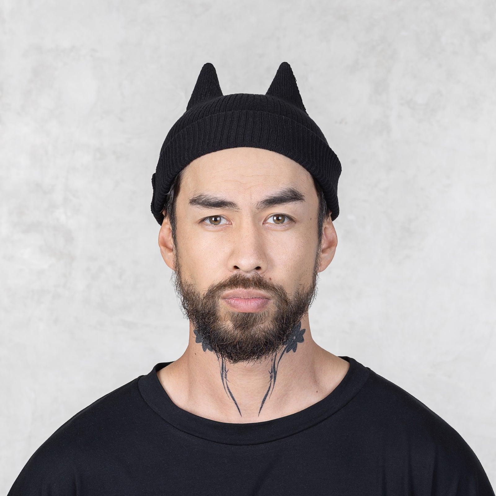 Man wearing a black knit beanie with spike ears against a light gray background