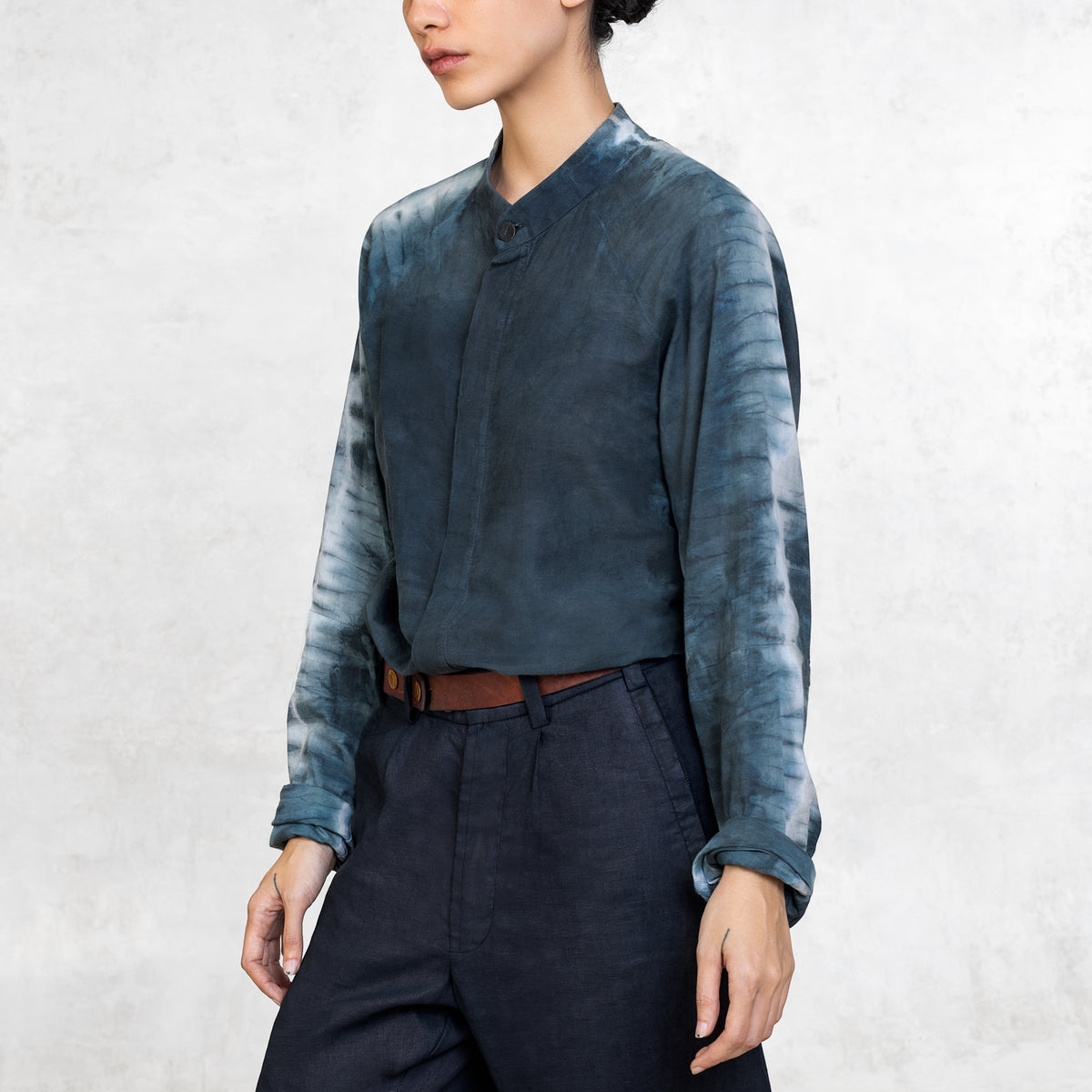 A woman in an tie-dyed indigo button up and Indigo linen pants from the thighs to the eyes