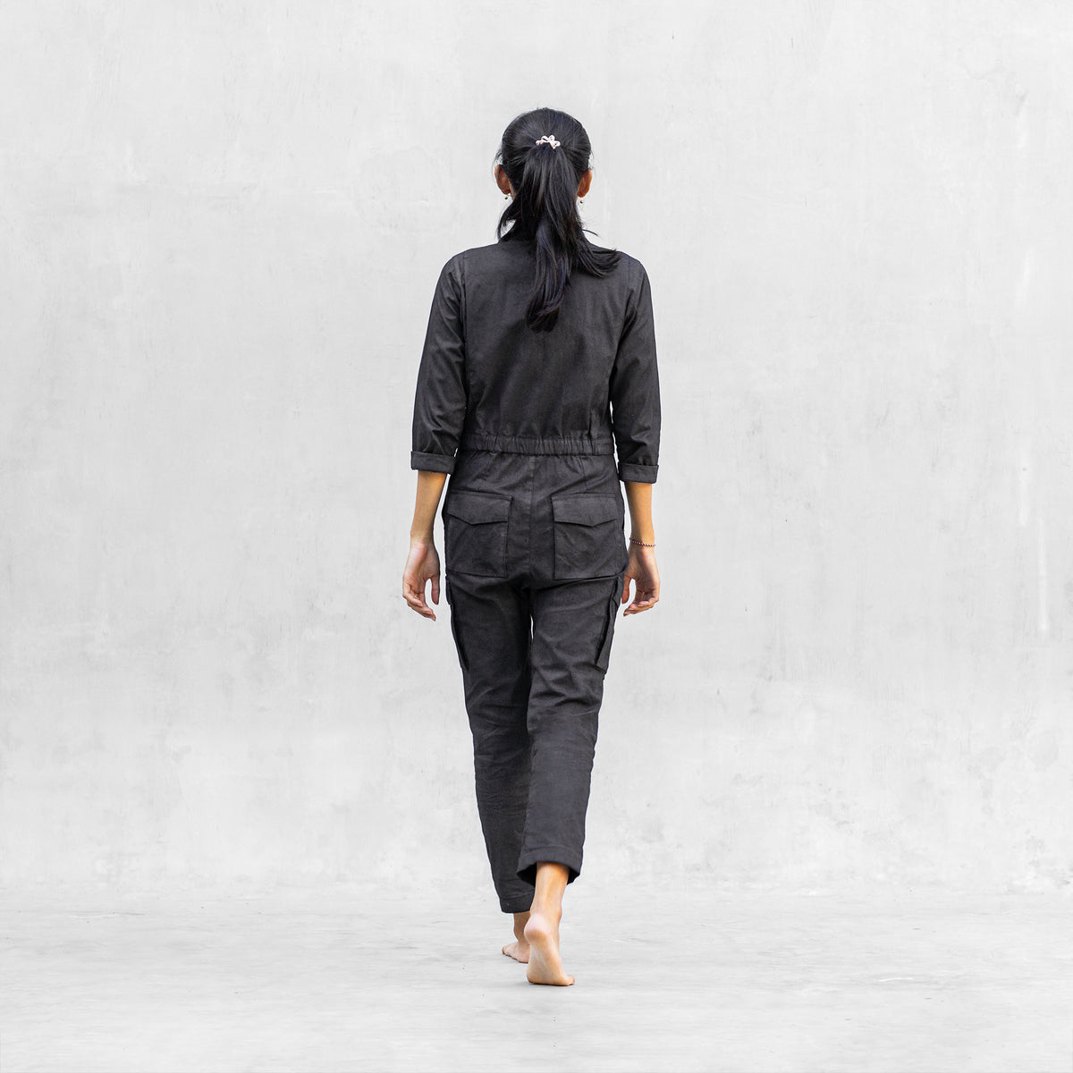 Woman walking from behind in a one piece black walnut mechanic style BLAMO jumpsuit 