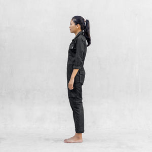 Woman standing sideways in a one piece black walnut mechanic style BLAMO jumpsuit 