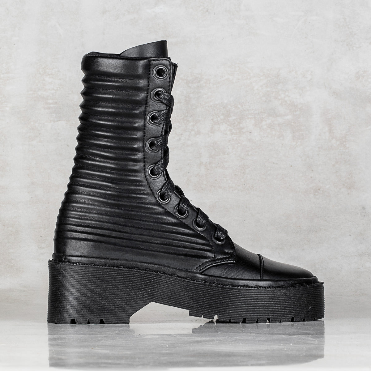A single black leather lace-up ankle boot with a chunky platform sole, ribbed shaft, and glossy finish, shown in a side profile against a textured light gray background.