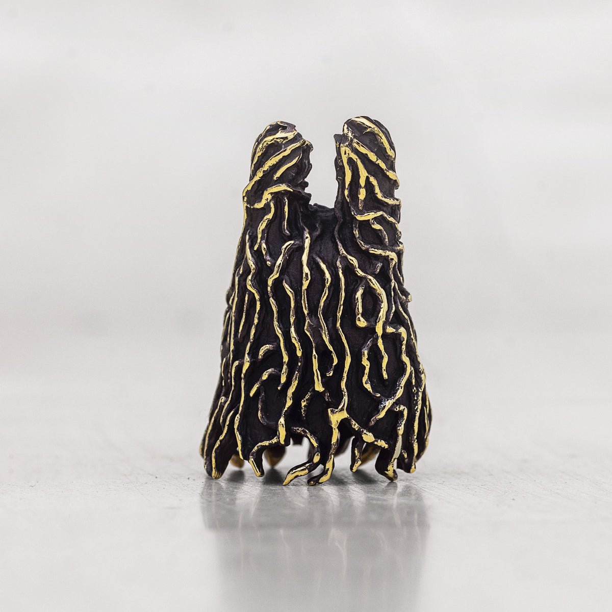 A black textured sculptural figurine with gold vein-like detailing, shown on a neutral light gray background.