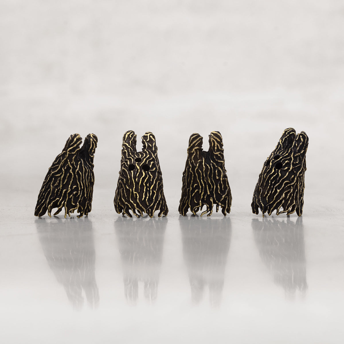 Four small black-and-gold striped figurines standing in a row on a reflective light gray surface against a soft gray background.