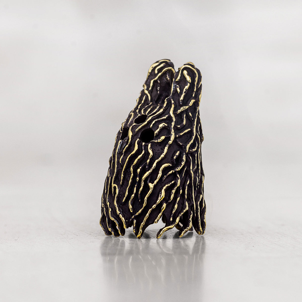 A small sculptural figurine detailed with gold wavy stripes on a black textured background, standing on a reflective light gray surface.