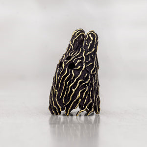 A small sculptural figurine detailed with gold wavy stripes on a black textured background, standing on a reflective light gray surface.