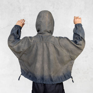 Person with their arms up facing back  wearing a hand painted olive windbreaker jacket and black pants against a white background. 