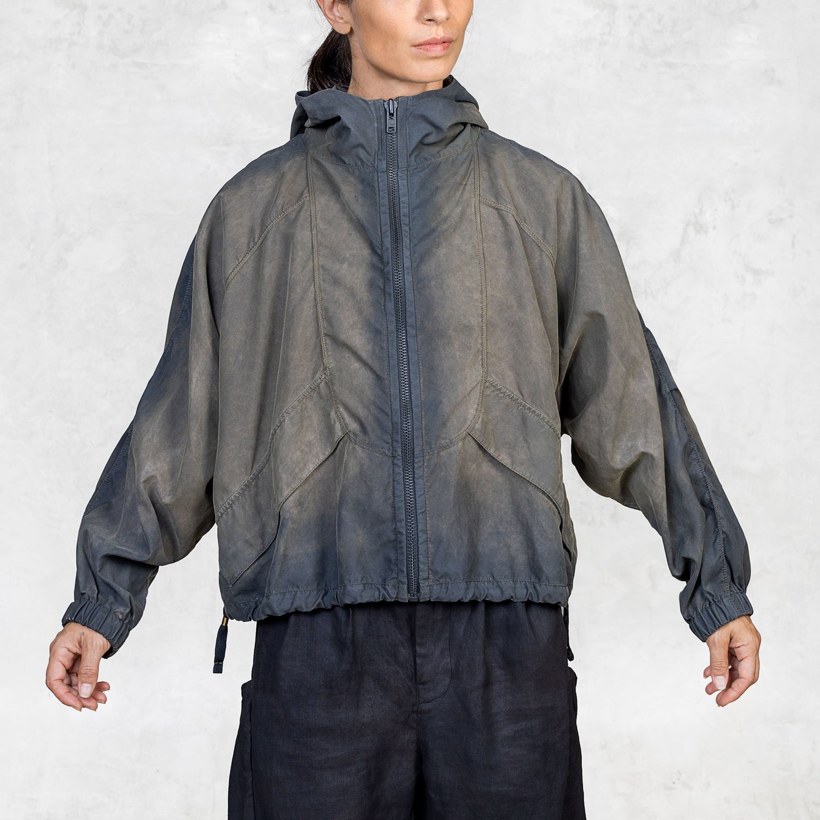 Person with their arms out wearing a hand painted olive windbreaker jacket and black pants against a white background. 