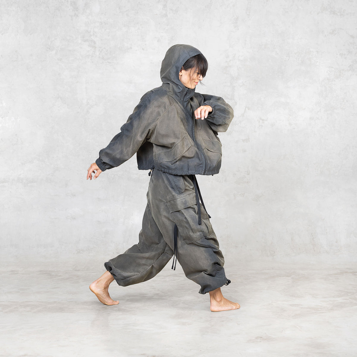 Person stepping sideways wearing a painted olive jacket and pants on a plain background