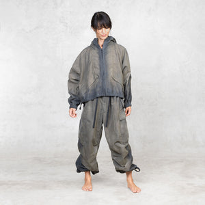 Person looking down wearing a painted olive jacket and pants on a plain background