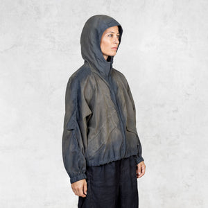 Person looking away wearing a hand painted olive windbreaker jacket and black pants against a white background. 
