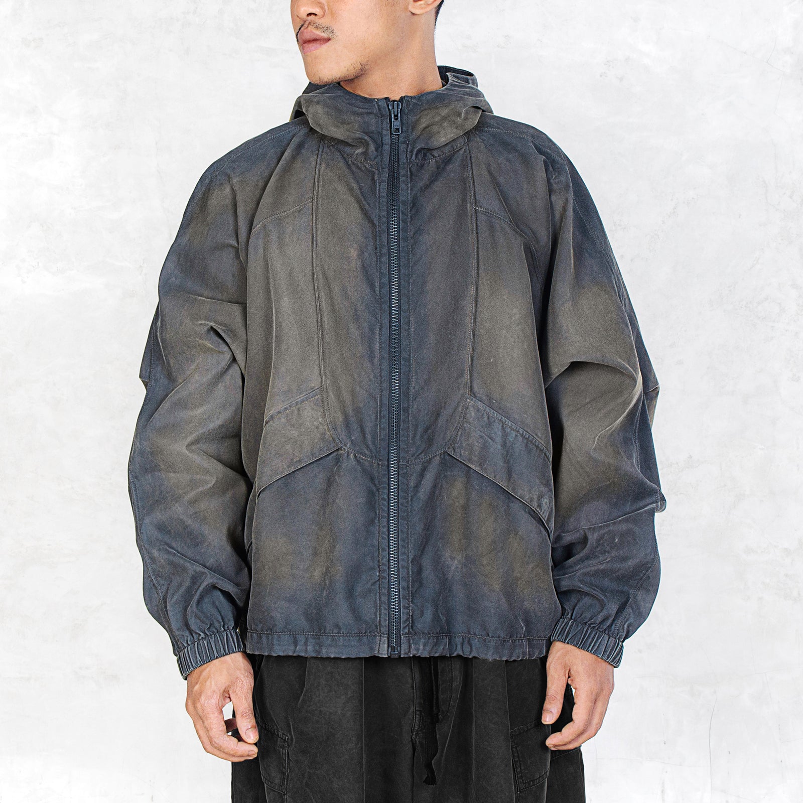 Person facing forward wearing a dark olive zip up jacket against a light grey background.