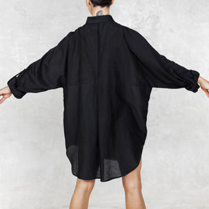 Person facing backwards wearing a black oversized shirt against a light gray background