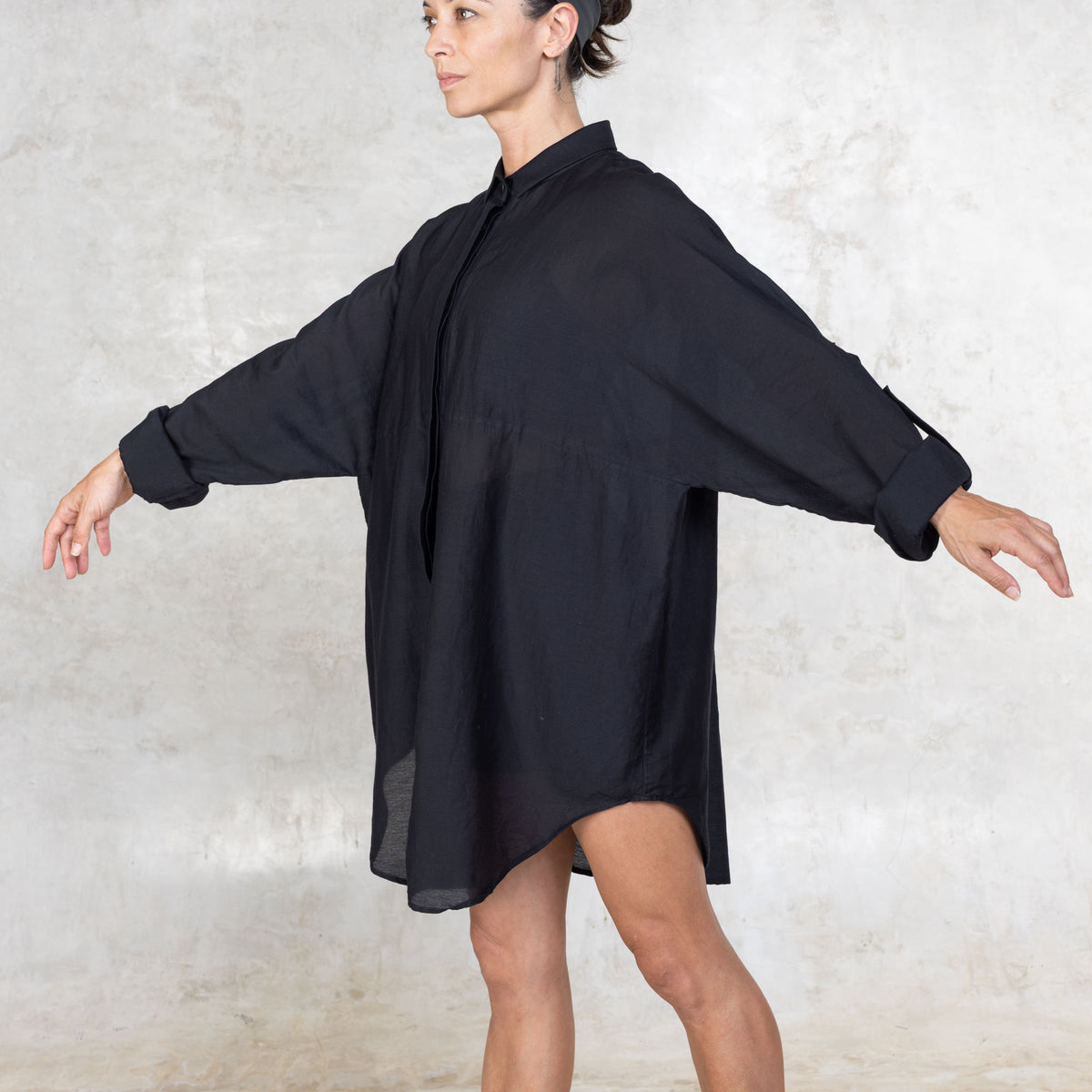 Person with their arms raised wearing a black shirt dress against a textured white background