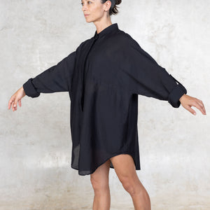 Person with their arms raised wearing a black shirt dress against a textured white background