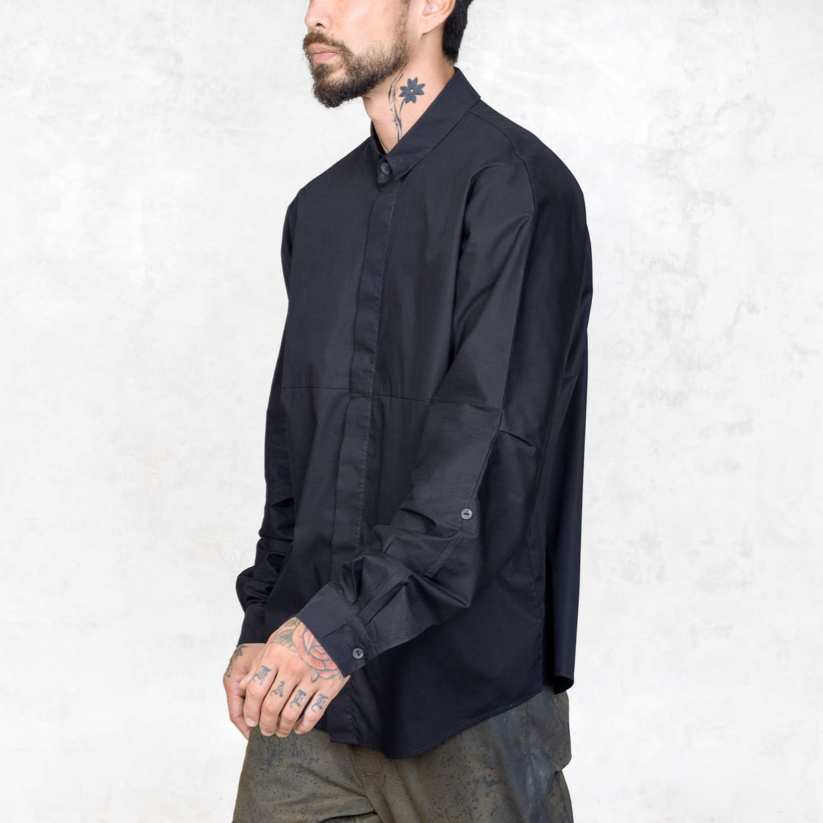 Person with tattoos wearing a black shirt against a white background