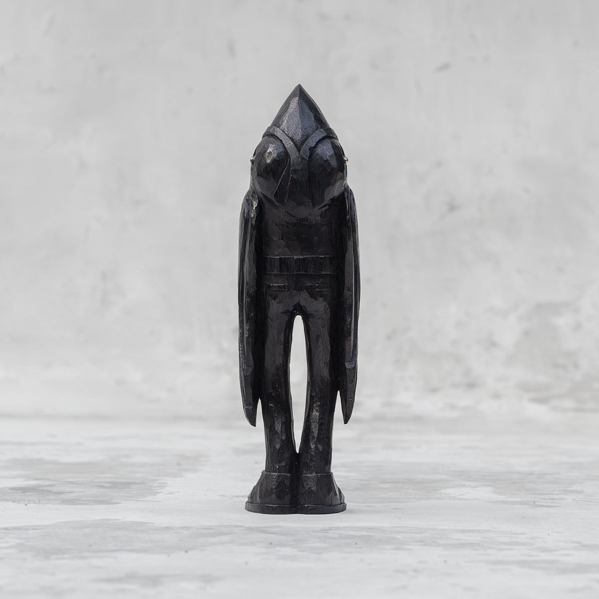 Back view of a black wooden raven person statuette  against a light gray background
